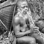 This woman smokes a pipe while taking a break from working on her farm outside Eshobi village, Cameroon. 1966.